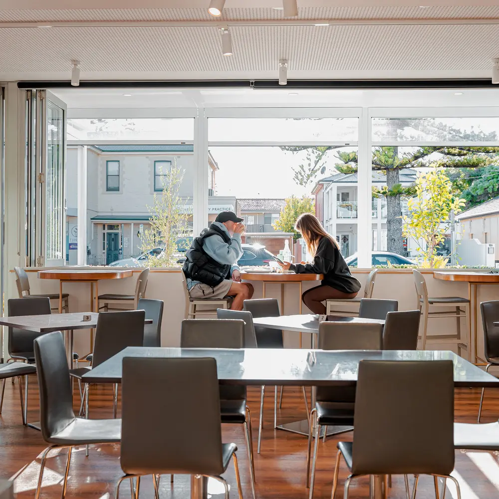 Inside of the Mediterranean Cafe Ristorante with two people drinking a coffee and the sunlight beaming through an open window onto tables and chairs. It was completely renovated by NDK constructions.